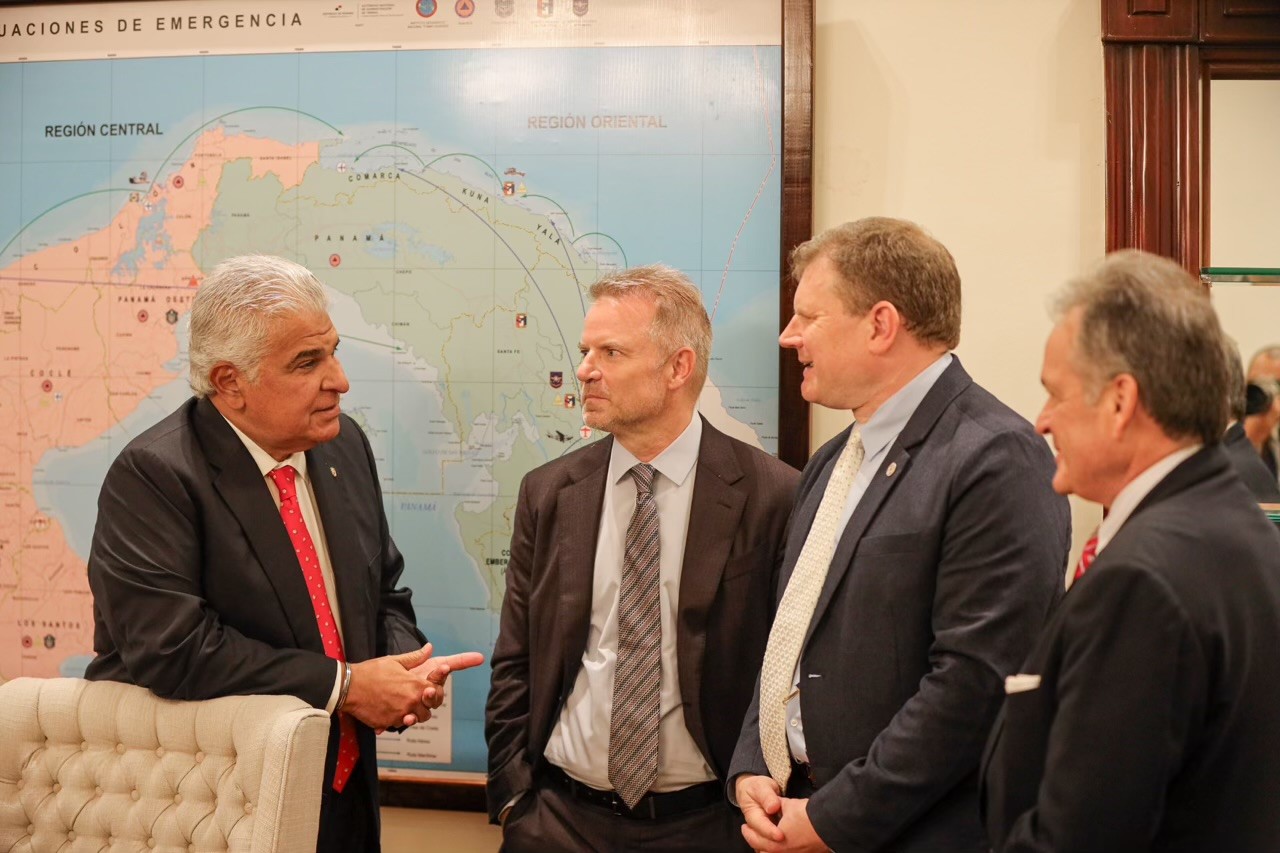 4 men in suits standing in conversation in front of a map of the Panama Canal region