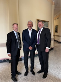 Three men standing side by side wearing suits and smiling into the camera.
