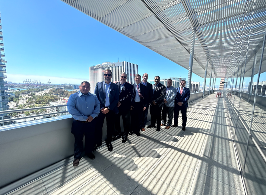 A group of men in suits standing on the balcony of a high-rise building overlooking the city and waterway.