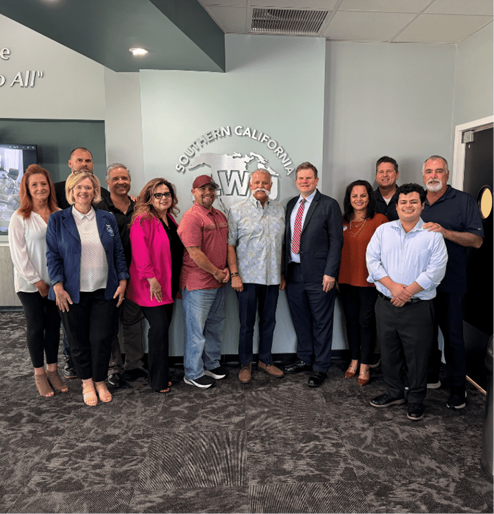 A group of men and women standing inside a building in Southern California smiling at the camera.