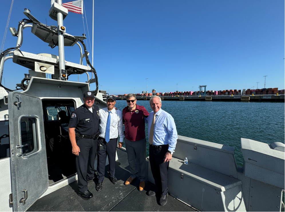 Four men on a U.S. Coast Guard Boat. One of the men is in an officer uniform. The boat is on a waterway.