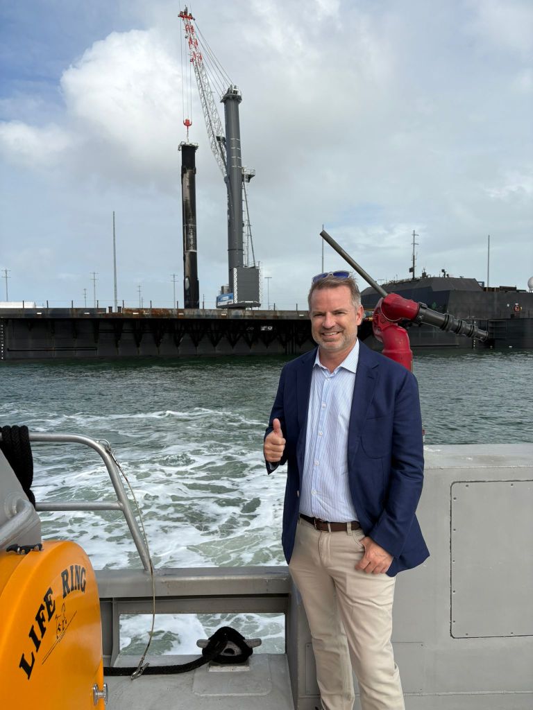 Man standing in front of a space launch platform smiling with his thumb up.