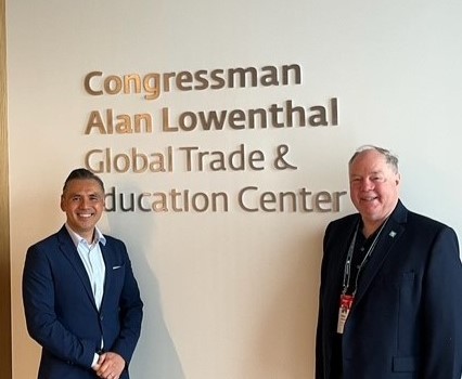Two men in suits standing on either side of a sign that reads "Congressman Alan Lowenthal Global Trade & Education Center".