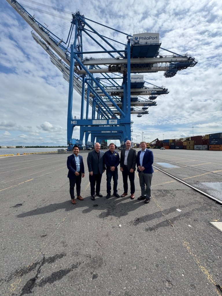 Five men standing at a port in front of cranes that says PhilaPort.