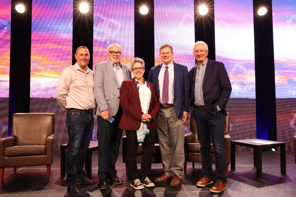 Five individuals on a stage posing for a photo with smiles.