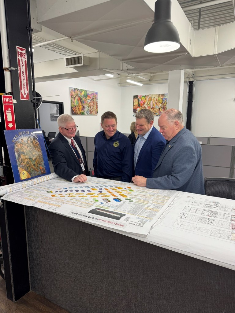 Four men looking down at a large poster document.